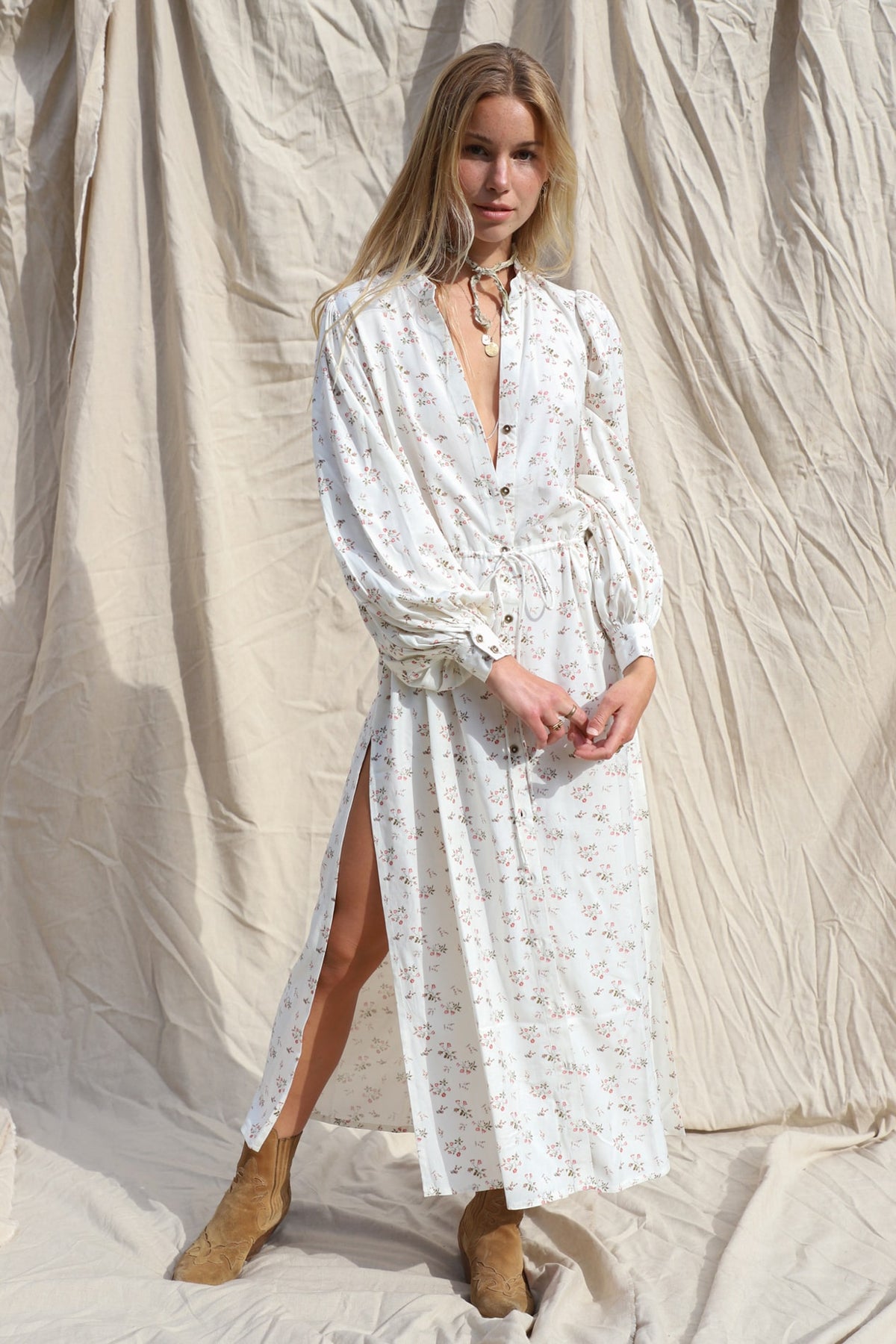white, floral, button up maxi dress with dual side slits, and adjustable tie at the waist, and long, blouson sleeves that end in a 2 button cuff